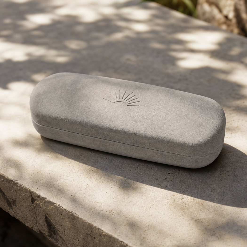 Closed suede-textured eyewear case on a sunlit stone surface